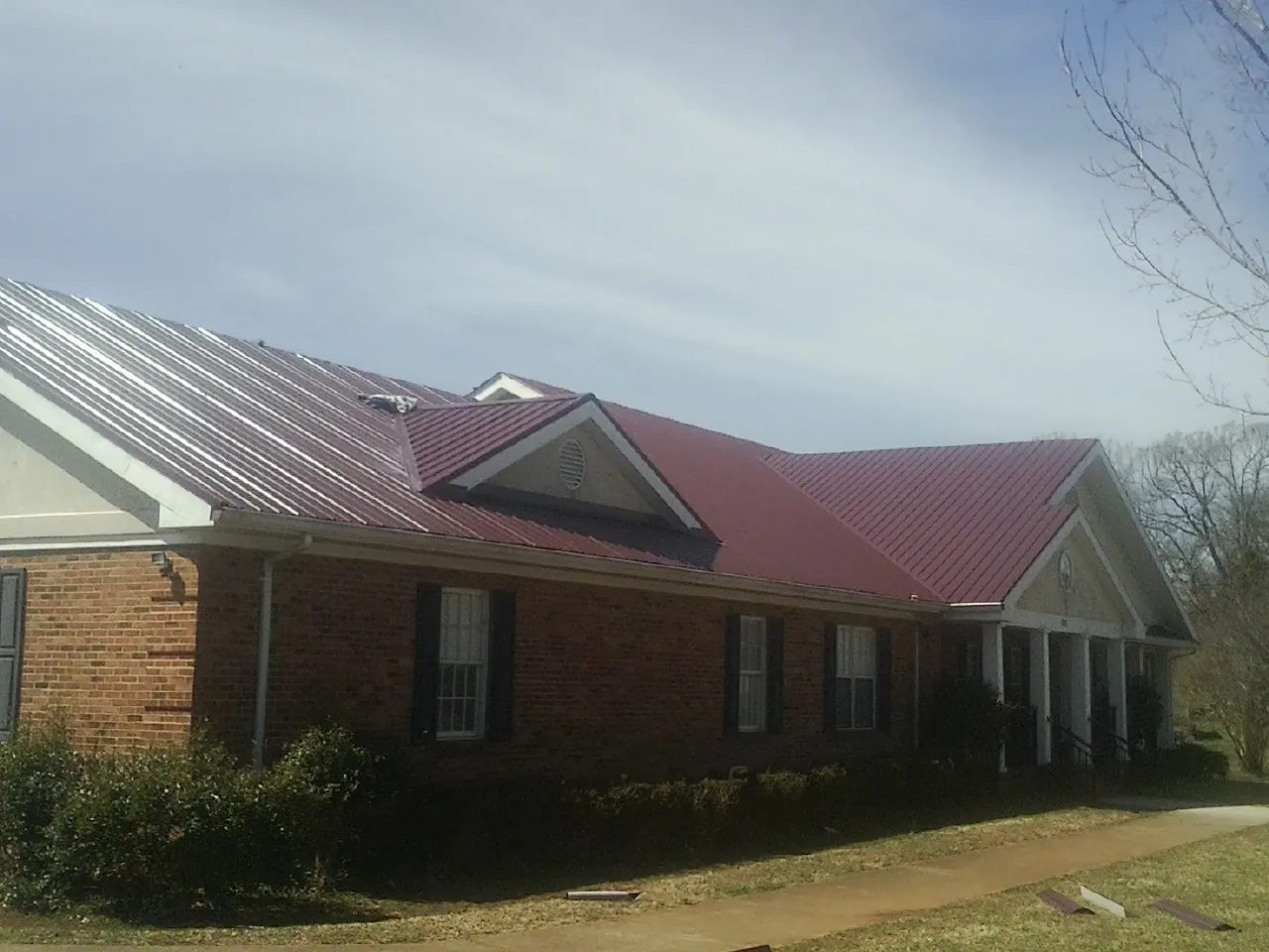 Red metal roof with gabled entries on a long brick building, from a Hail Damage Roof Repair job in Pine Hill