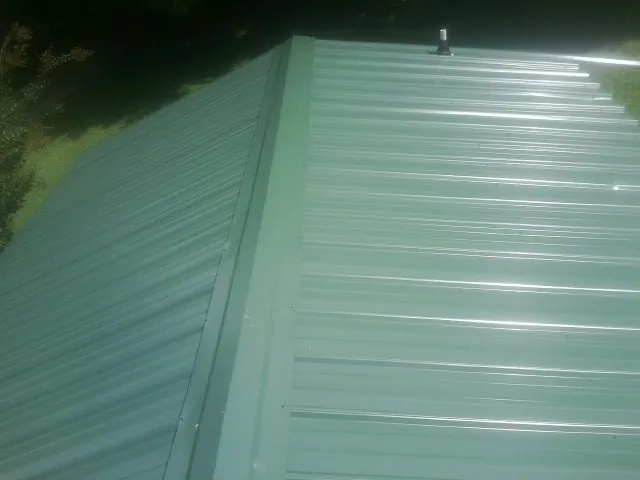 New green metal panels meeting at the ridge of a roof — Flat Roof Repair work by our crew in Pine Hill