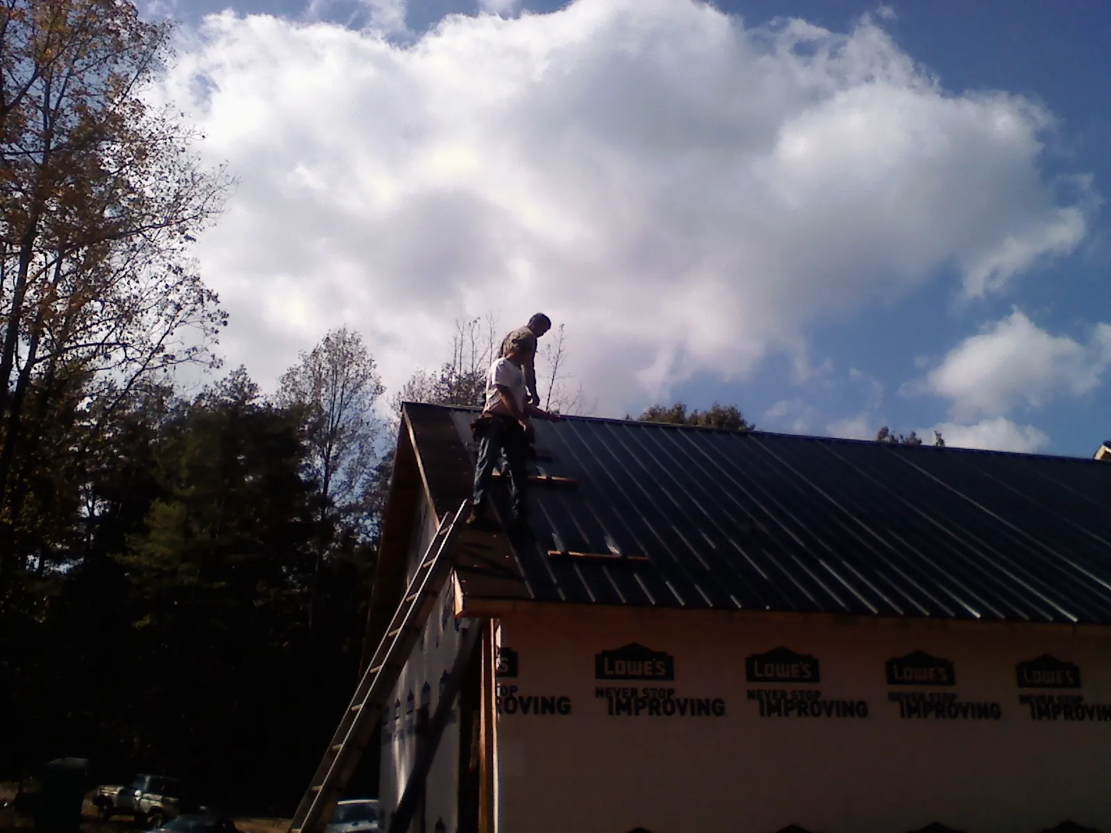 Roofer fastening dark metal panels high against a cloudy sky, from a Roof Inspection job in Pine Hill