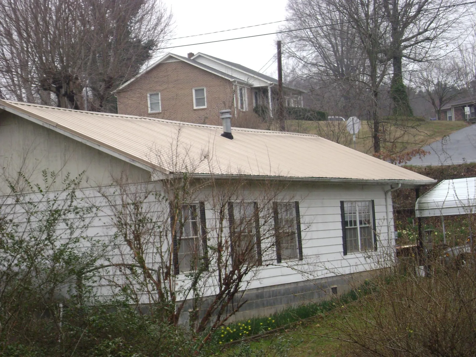 Tan metal roof on a white sided house set into a hillside — Commercial Roofing by Roofing Brothers in Pine Hill